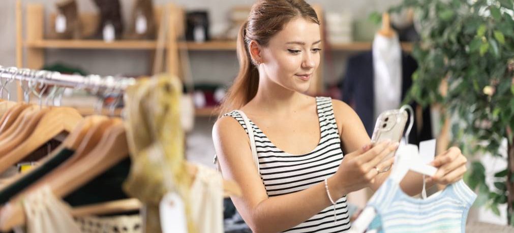 Young woman scans the QR code of labels in a clothing store on mobile, she reads detailed information about the manufacturer. Customer uses mobile app payment