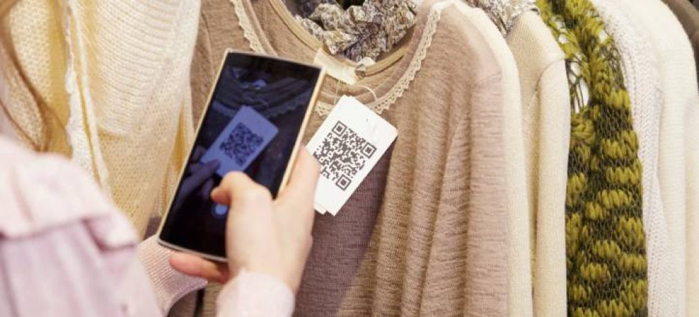 Woman scanning a QR code, with her smart phone, from a label in a clothing store. No face.